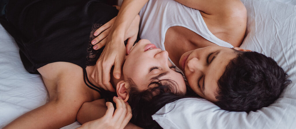 image of two women in bed. One is has her hand placed on the others throat.